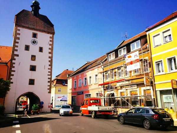 Historischer Stadtturm mit Uhr und Wohnhäusern, Baugerüst und Autos in sonniger Altstadt.