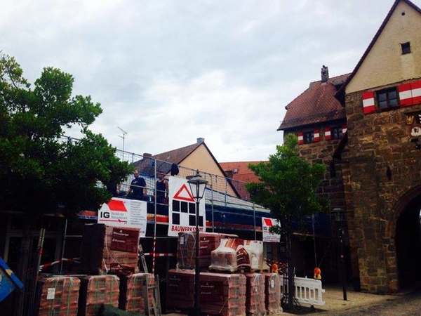 Sanierungsarbeiten an einer historischen Stadtmauer mit Baugerüst, Baumaterial und Arbeitern.